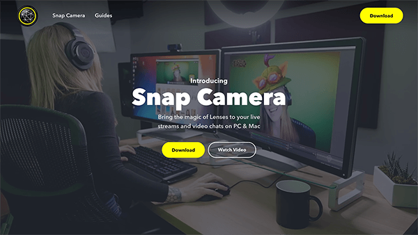 Esta es una captura de pantalla del sitio web de Snap Camera. En el fondo de la página, una mujer se sienta frente a una computadora de escritorio con auriculares y usa una lente de realidad aumentada para que parezca que lleva un sombrero tonto y caricaturesco. El texto blanco en el centro de la página dice "Lleva la magia de las lentes a tus transmisiones en vivo y chats de video en PC y Mac". Un botón amarillo tiene la etiqueta Descargar.